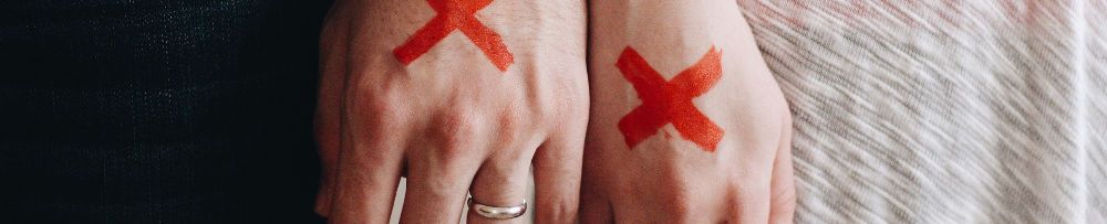 Scheidung: Mann und Frau mit Ehering und roten Kreuzen auf der Handrückseite